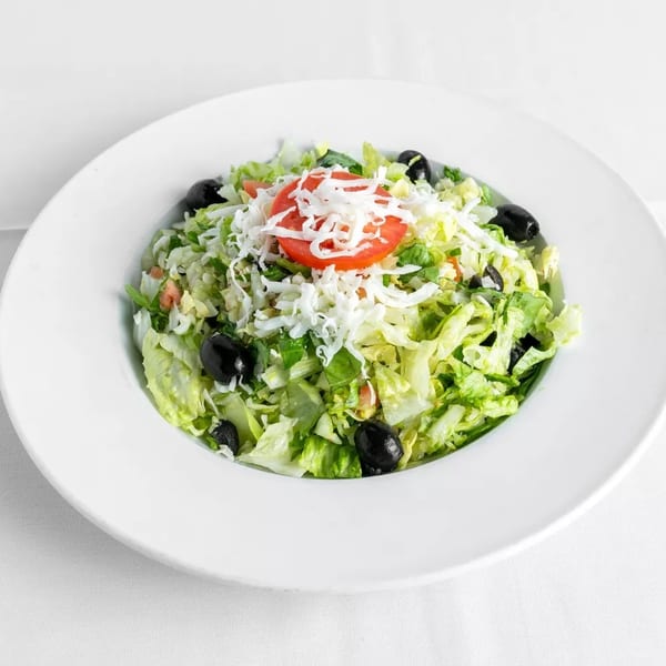 A fresh garden salad with lettuce, black olives, shredded cheese, and a tomato slice in a white bowl.