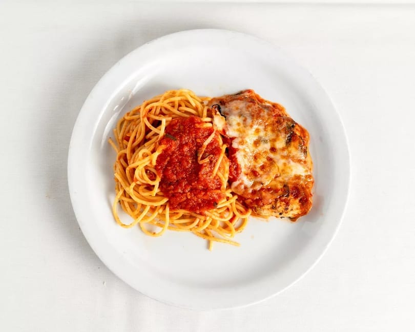 Chicken parmesan with melted cheese and spaghetti with red sauce on a white plate.