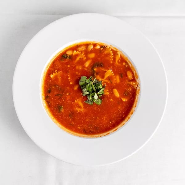 Minestrone soup with pasta, beans, and greens, garnished with fresh herbs in a white bowl.