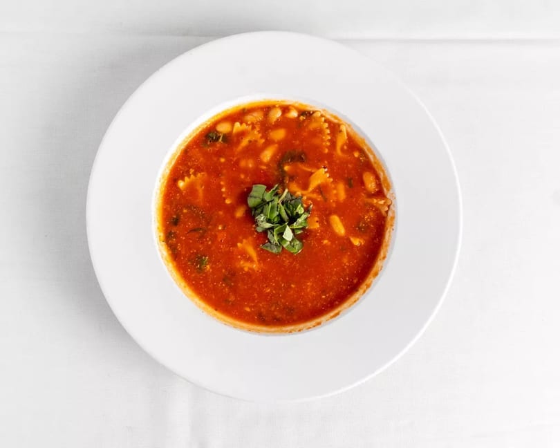 Minestrone soup with pasta, beans, and greens, garnished with fresh herbs in a white bowl.