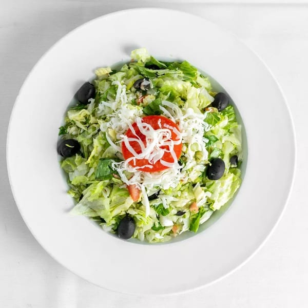 Fresh green salad with shredded cheese, sliced tomatoes, and black olives in a white bowl.