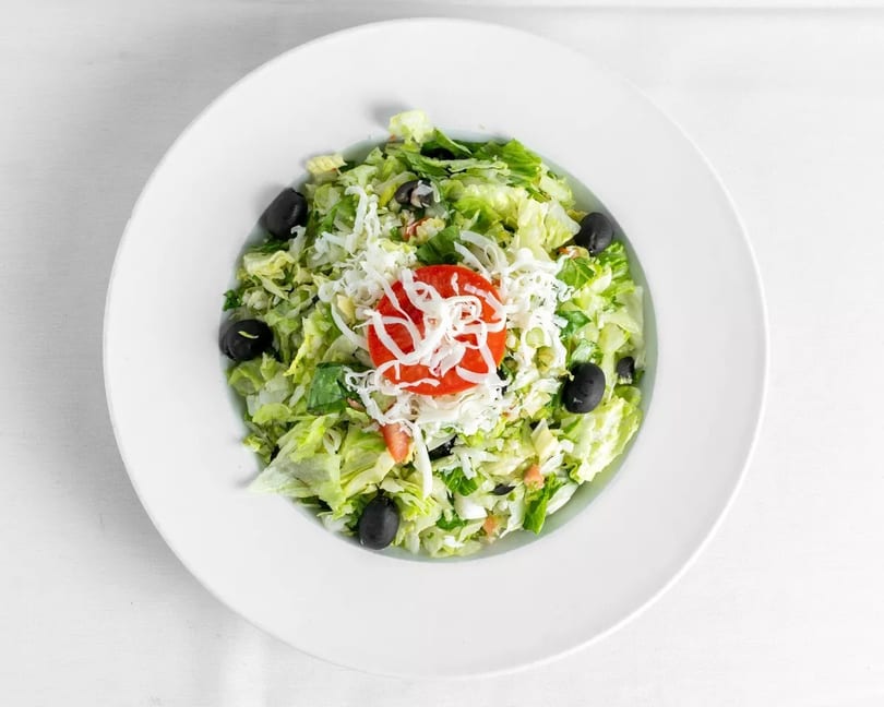 Fresh green salad with shredded cheese, sliced tomatoes, and black olives in a white bowl.