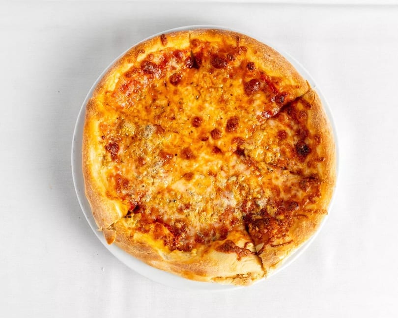 A whole cheese pizza with a golden crust, cut into slices, on a white plate.