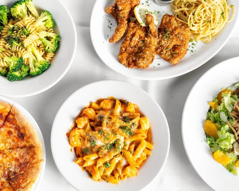 An overhead view of various Italian dishes, including pasta with broccoli, fried chicken, pizza, and salad.