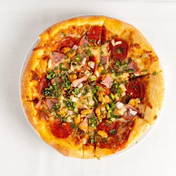 A whole pizza with pepperoni, ham, onions, green peppers, and cilantro on a white plate.