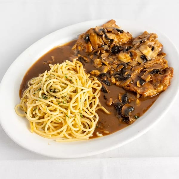 Chicken Marsala with mushrooms and gravy, served alongside a pile of spaghetti on a white plate.