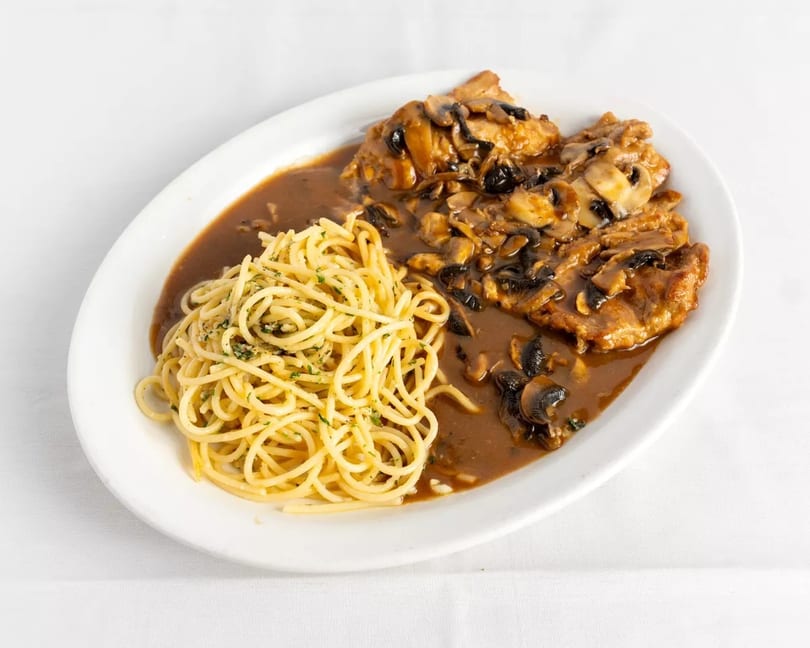 Chicken Marsala with mushrooms and gravy, served alongside a pile of spaghetti on a white plate.