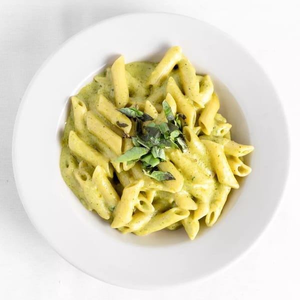 Penne pasta with creamy green pesto sauce and fresh basil in a white bowl.