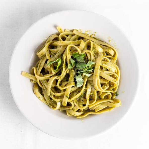 Fettuccine pasta with green pesto sauce and fresh basil in a white bowl.