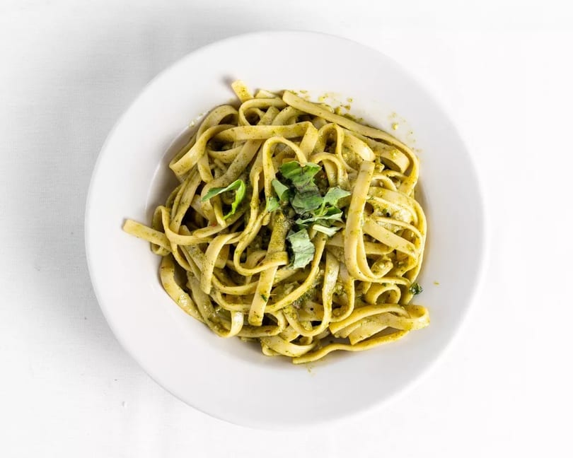 Fettuccine pasta with green pesto sauce and fresh basil in a white bowl.