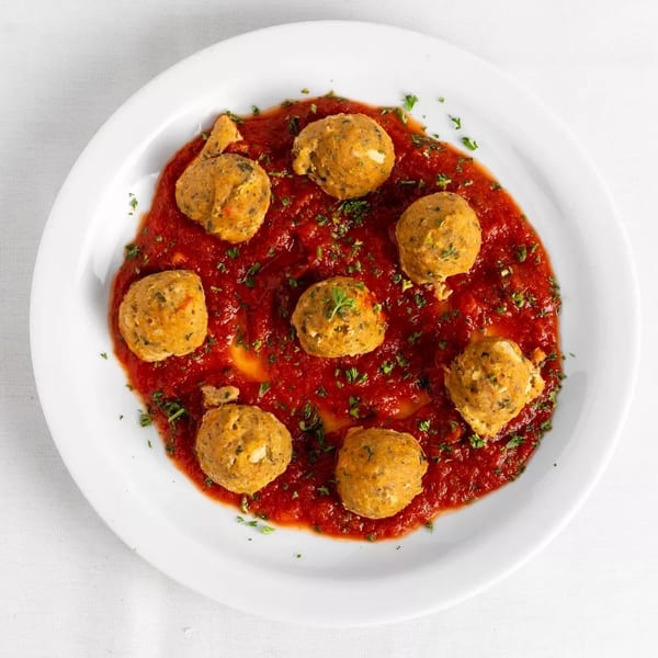 Seven golden-brown meatballs in a rich red tomato sauce, garnished with fresh parsley on a white plate.
