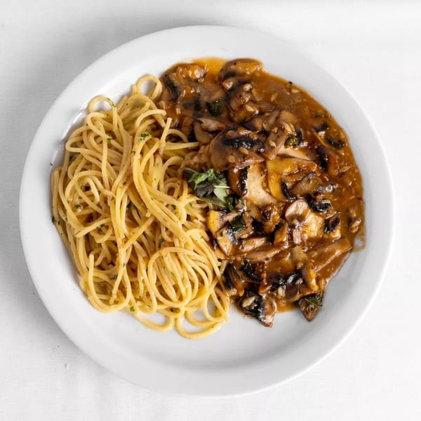 Spaghetti with mushroom sauce and herbs on a white plate, viewed from above.