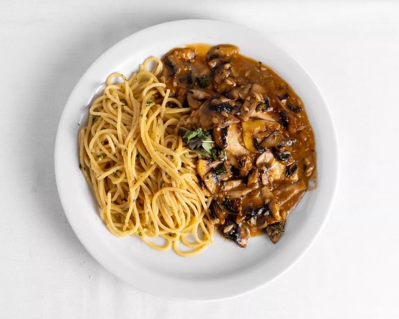 Spaghetti with mushroom sauce and herbs on a white plate, viewed from above.