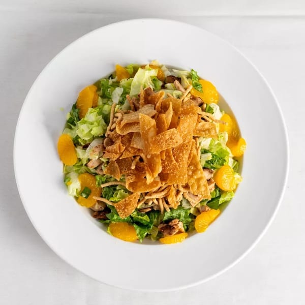 Overhead view of a vibrant salad with lettuce, mandarin oranges, and crispy wonton strips in a white bowl.