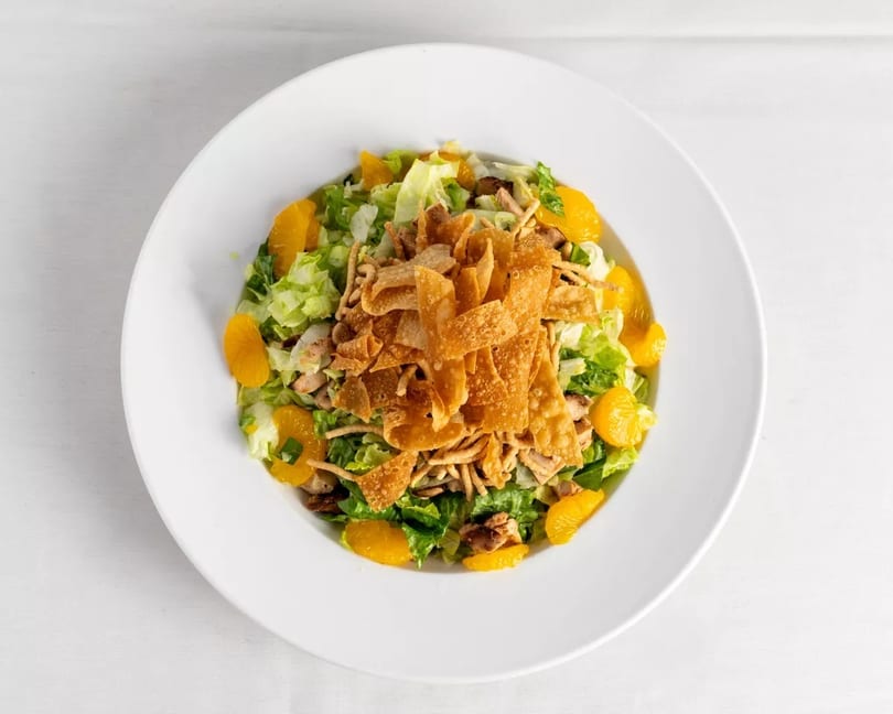 Overhead view of a vibrant salad with lettuce, mandarin oranges, and crispy wonton strips in a white bowl.