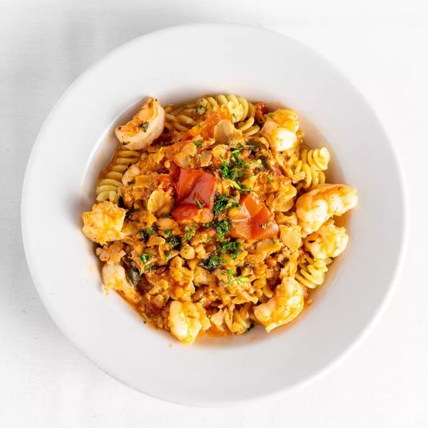 Close-up of fusilli pasta with shrimp, clams, and red sauce, garnished with parsley.