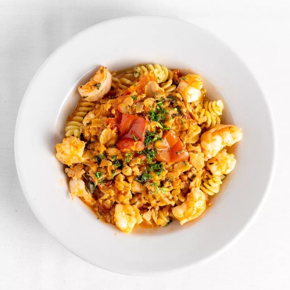Close-up of fusilli pasta with shrimp, clams, and red sauce, garnished with parsley.