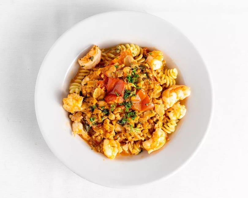 Close-up of fusilli pasta with shrimp, clams, and red sauce, garnished with parsley.